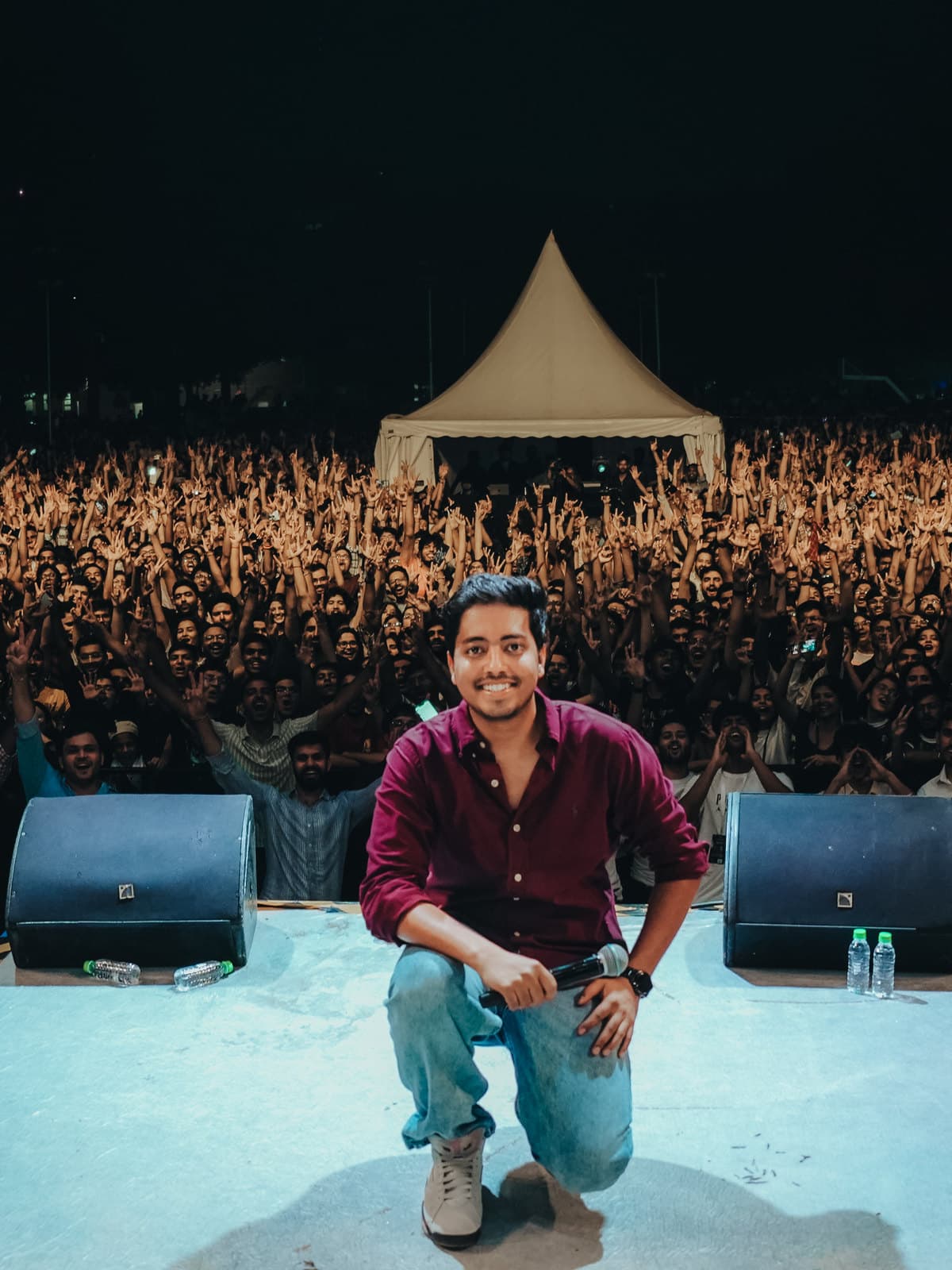 A performer crouched at the edge of the stage, the crowd filling the ground behind