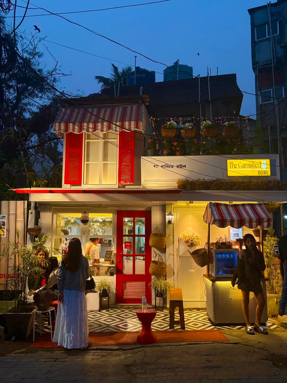 A small café with red shutters, lit up at dusk