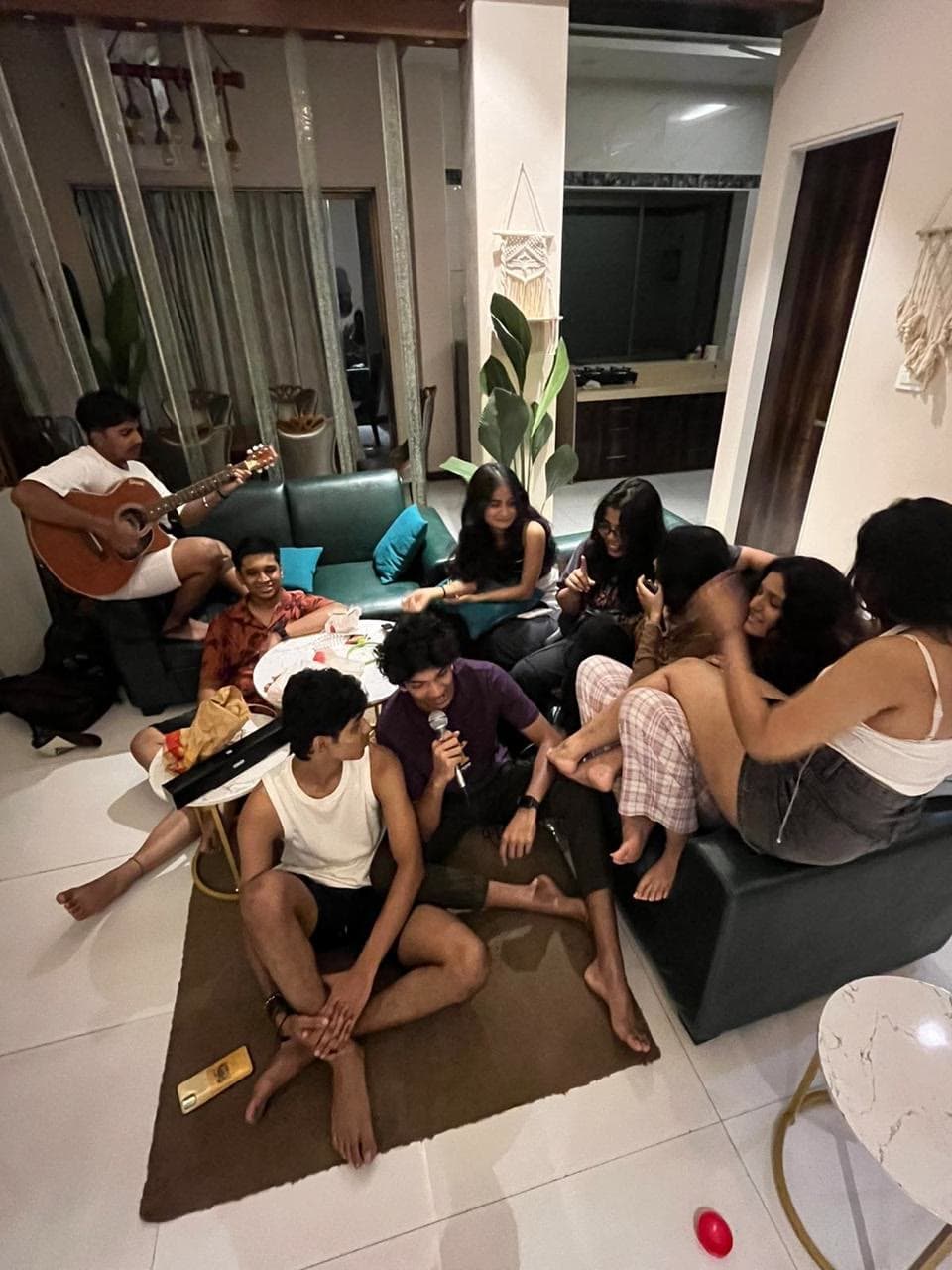 The group sprawled around a living room at night, one on a guitar, one singing