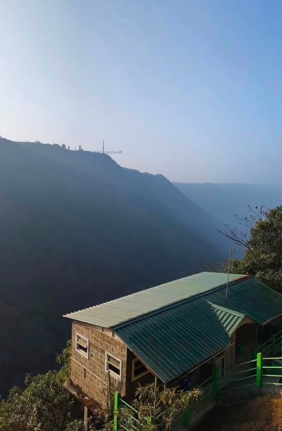 A green-roofed shack perched on a hillside above a deep valley