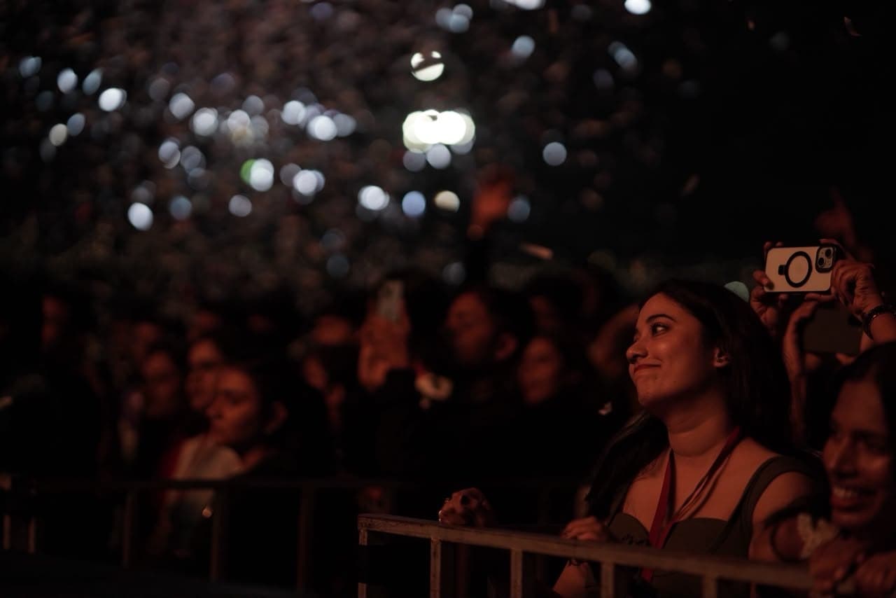 A student at the front barricade watching the stage, the crowd lit behind her