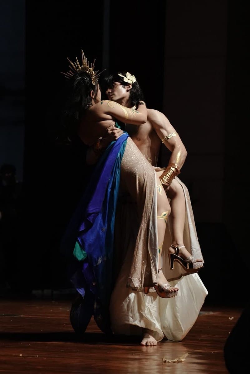 Two dancers mid-lift in gold costume under a stage spot