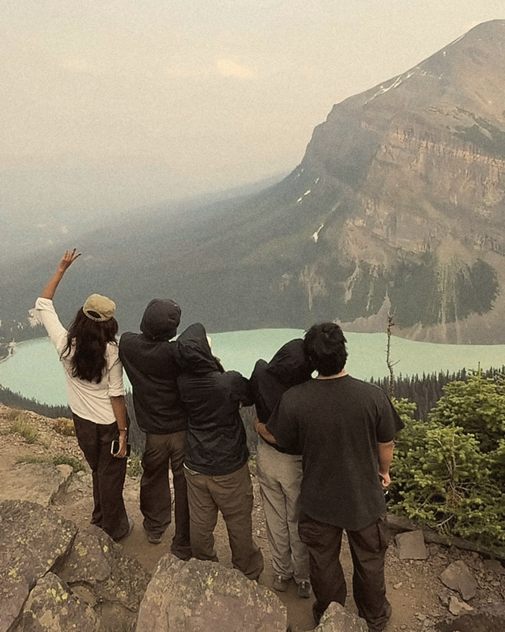 Friends waving at a turquoise lake from a mountain ledge