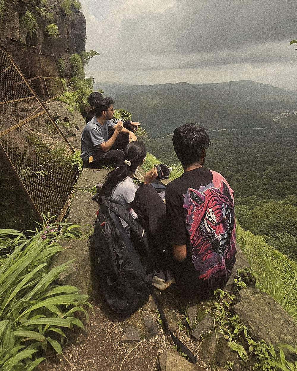 Friends sitting on a cliff ledge above a green valley
