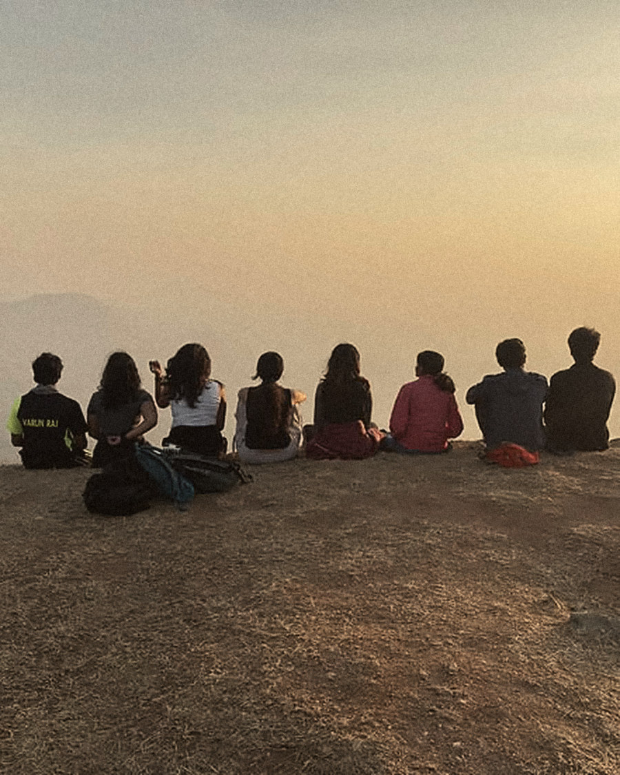 Friends sitting in a row on a hilltop at sunset